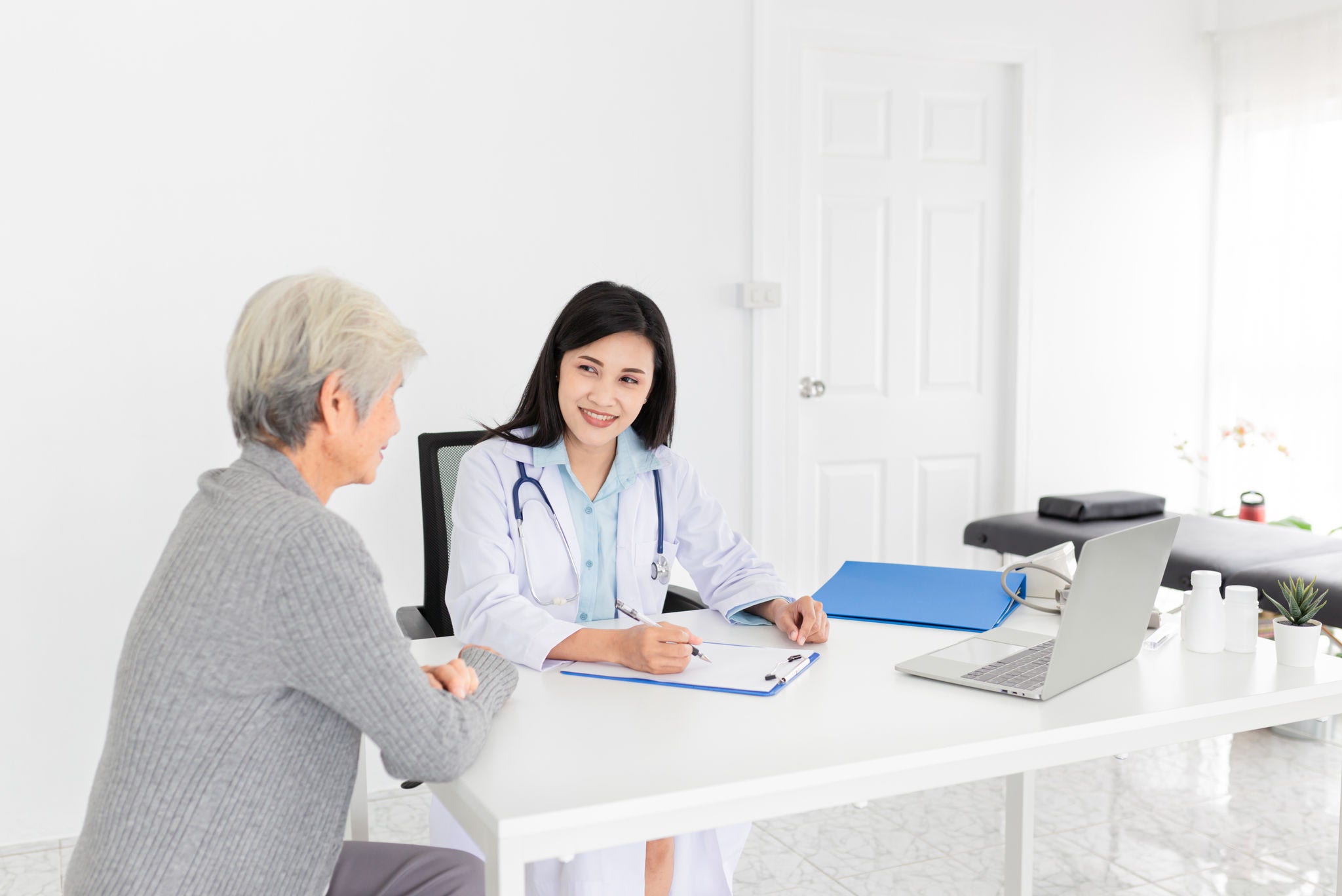 asian female doctor talk with old patient in mental health clinic, she screening and write patient information on patient chart, elderly healthcare promotion; Shutterstock ID 1831611679; purchase_order: -; job: -; client: -; other: -