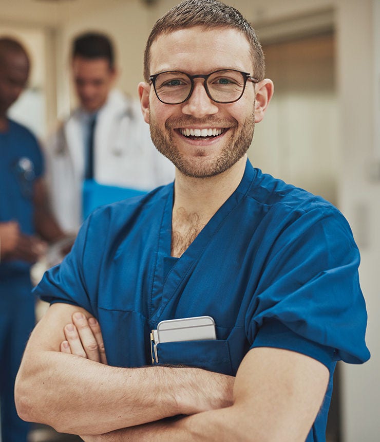 Smiling optimistic young male hospital surgeon standing in front of his colleagues with folded arms beaming at the camera; Shutterstock ID 432229576; purchase_order: -; job: -; client: -; other: -