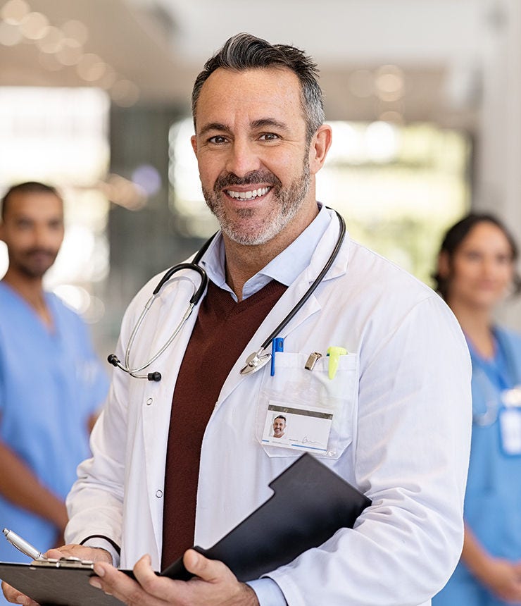 Portrait of mature doctor wearing lab coat and stethoscope reading patient case file in hospital. Successful head physician standing in hospital hallway and looking at camera with his medical team.; Shutterstock ID 2060102024; purchase_order: -; job: -; client: -; other: -