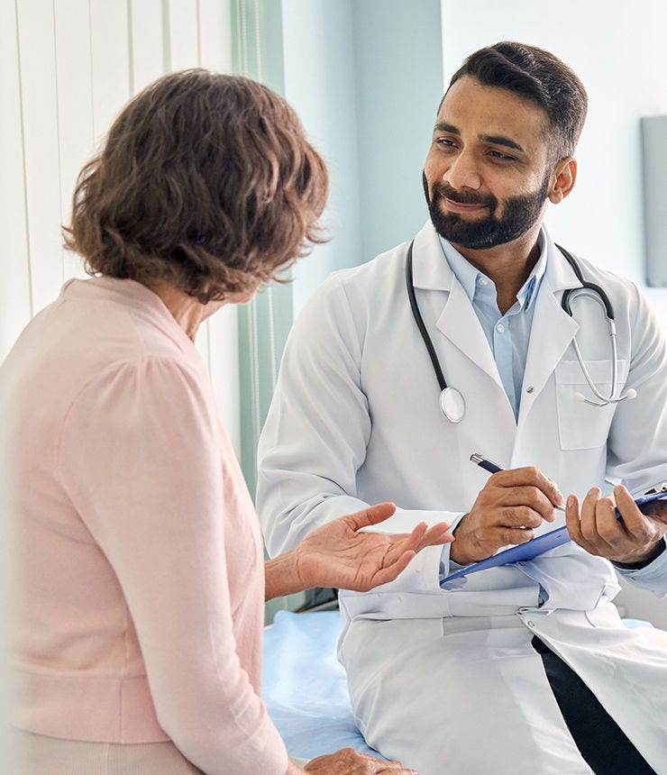 Indian male doctor consulting senior old patient filling form at consultation. Professional physician wearing white coat talking to mature woman signing medical paper at appointment visit in clinic.; Shutterstock ID 2036186195; purchase_order: -; job: -; client: -; other: -