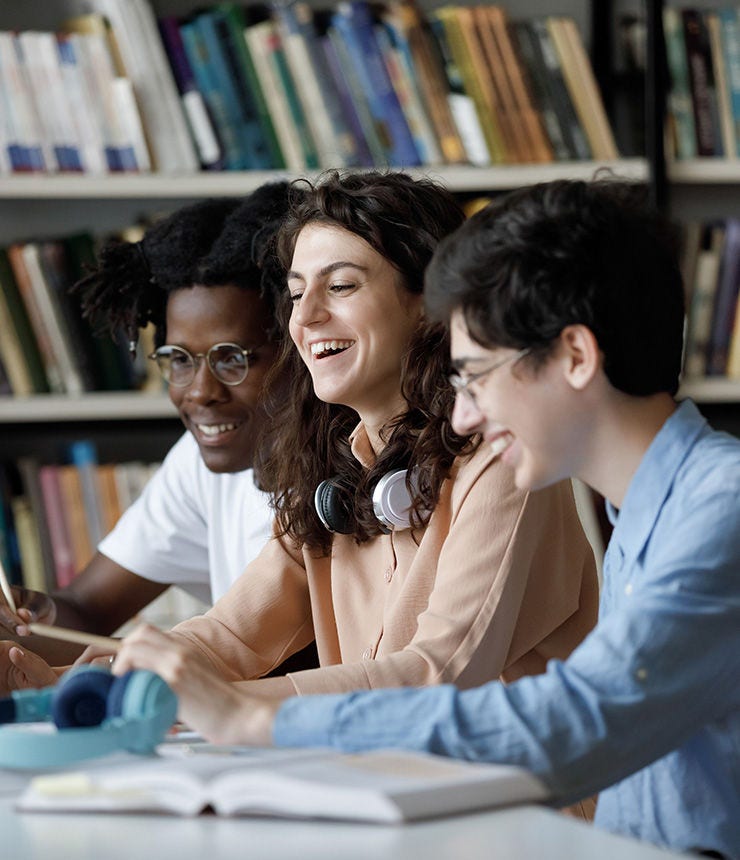 Laughing multi ethnic students use laptop studying or having fun using laptop sit at shared table in university library, having friendly relations, prepare for exams together using modern tech concept; Shutterstock ID 2139744927; purchase_order: -; job: -; client: -; other: -