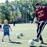 Regis College Children Center student playing soccer with a Regis College student