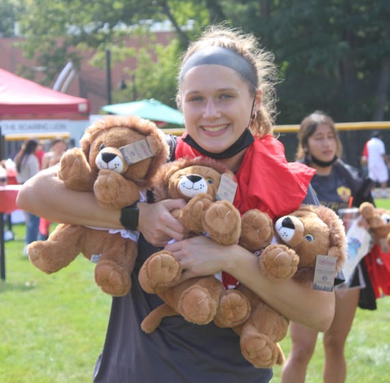 A smiling student holding three stuffed lions in her arms