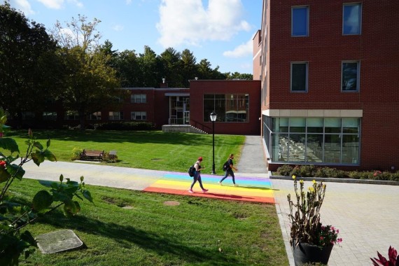 Two students walk across a rainbow-painted section of path in front of Maria Hall on the Weston campus
