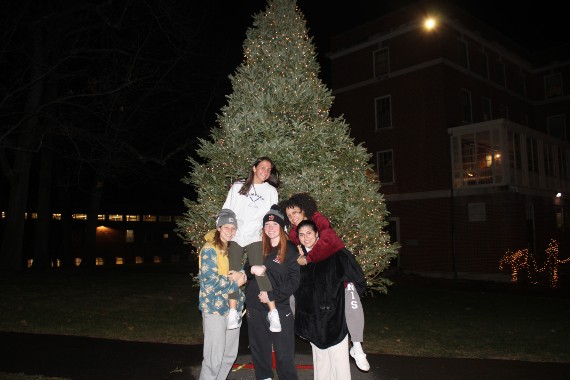 Three students holding two others on their shoulders in front of the Christmas tree on the Weston campus