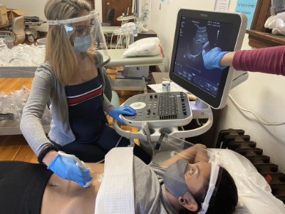 Lilyana Nunez, ’22, practices using an ultrasound machine on fellow diagnostic medical sonography students Lina Gonzalez, ’22. Both are wearing face shields made by assistant professor Brian Plouffe.