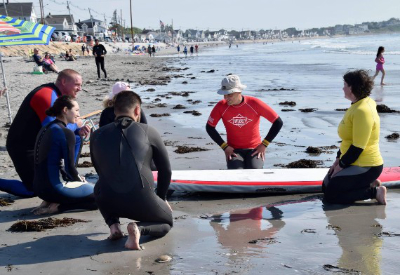 A group in wetsuits gathered around a surf board