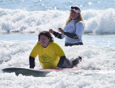 A woman in a yellow shirt rides a surf board