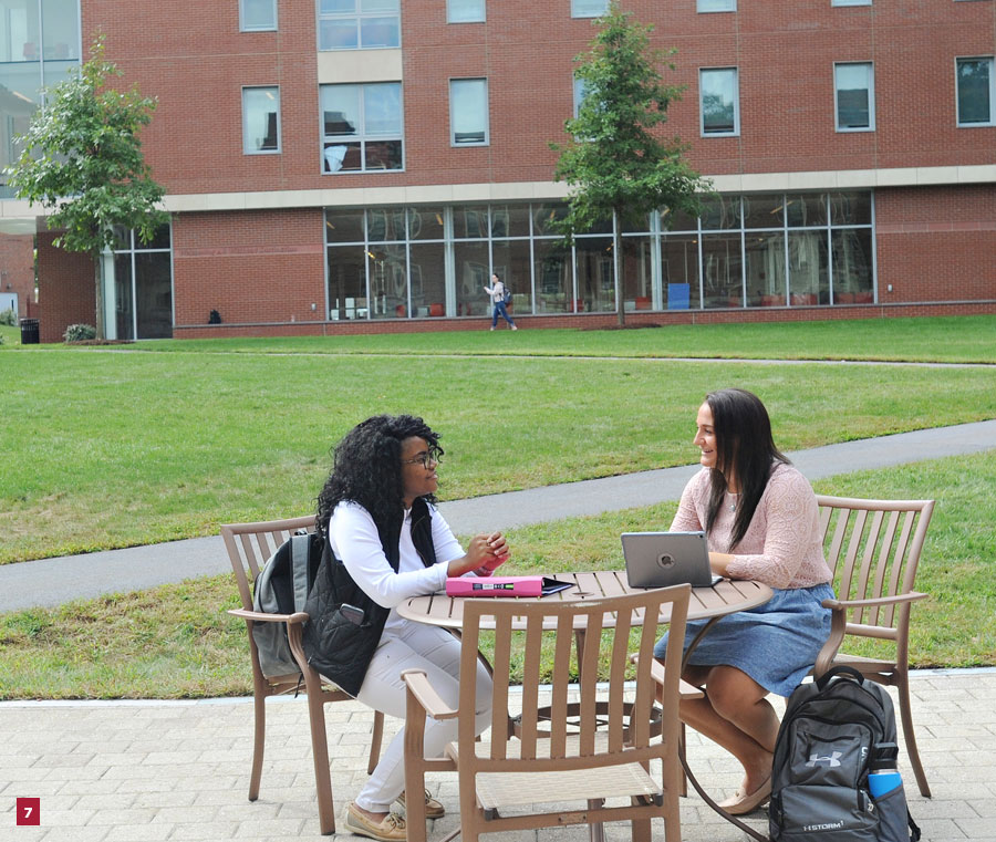 7) photo of two students sitting at a table in the Luben Plaza qith the Quad in the background