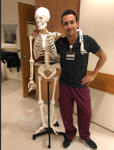 Brendan Kelley poses with a skeleton while dressed in scrubs.