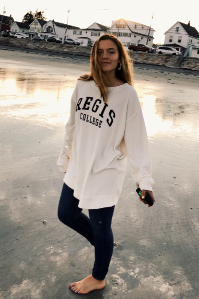 Sarah Ferguson ‘24 poses on a beach wearing a Regis College sweatshirt