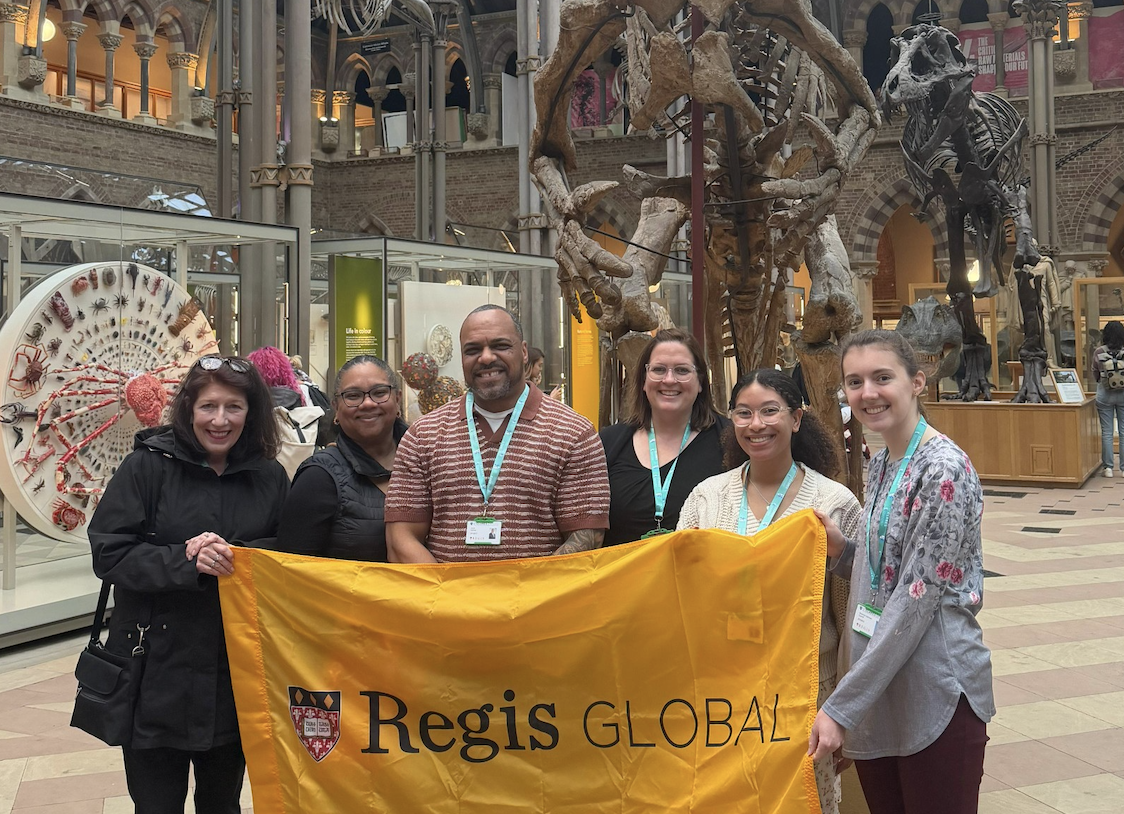 Students stand in front of a dinosaur skeleton while holding a yellow banner
