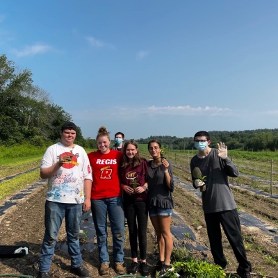A Student wearing a Regis shirt poses with high school students on a farm