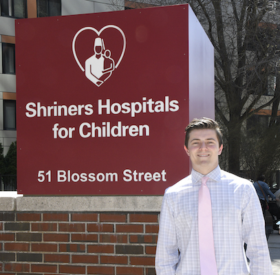 Genzale smiles in front of MGH Shriners sign