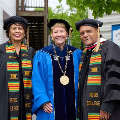 Three people wearing academic regalia and smiling directly at the camera