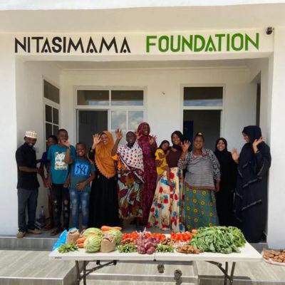 A group of people pose behind a table of fresh produce at Nitasimama Foundation