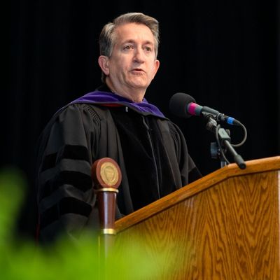A man speaking at a podium and wearing a graduation gown
