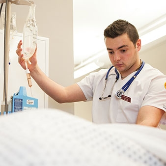 A nursing student with a stethoscope around his neck holding an IV bag
