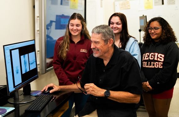 a professor surrounded by a group of students view a computer screen